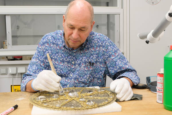 Restaurator Uwe Schuchardt säubert das vor ihm liegende Große Scheibenkreuz mit einem Pinsel. 