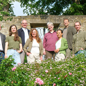 Foto des Umweltteams inmitten eines Gartens mit Rosen im Vordergrund, Bäumen und einer alten Mauer im Hintergrund