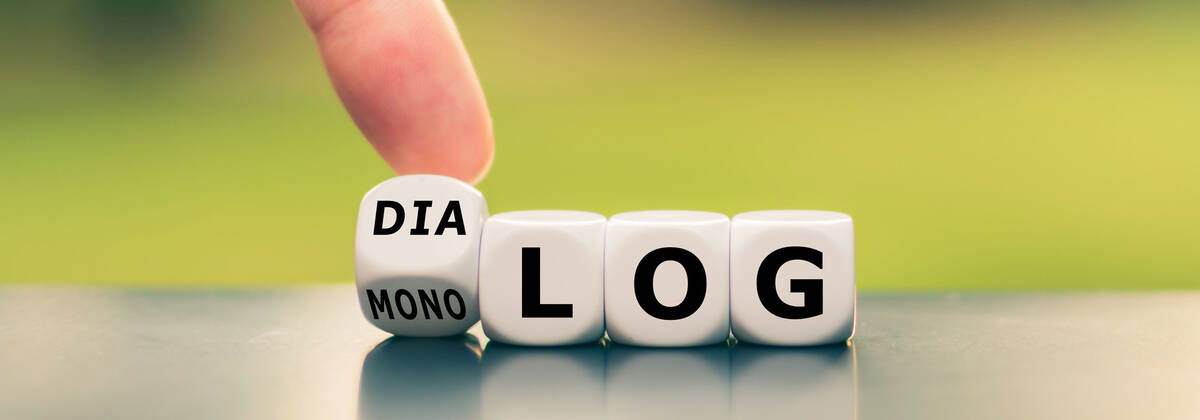 Link zur Seite Interreligiöser Dialog Symbolbild zum Interreligiösen Dialog: Hand dreht einen Würfel und ändert das Wort "Monolog" in "Dialog".