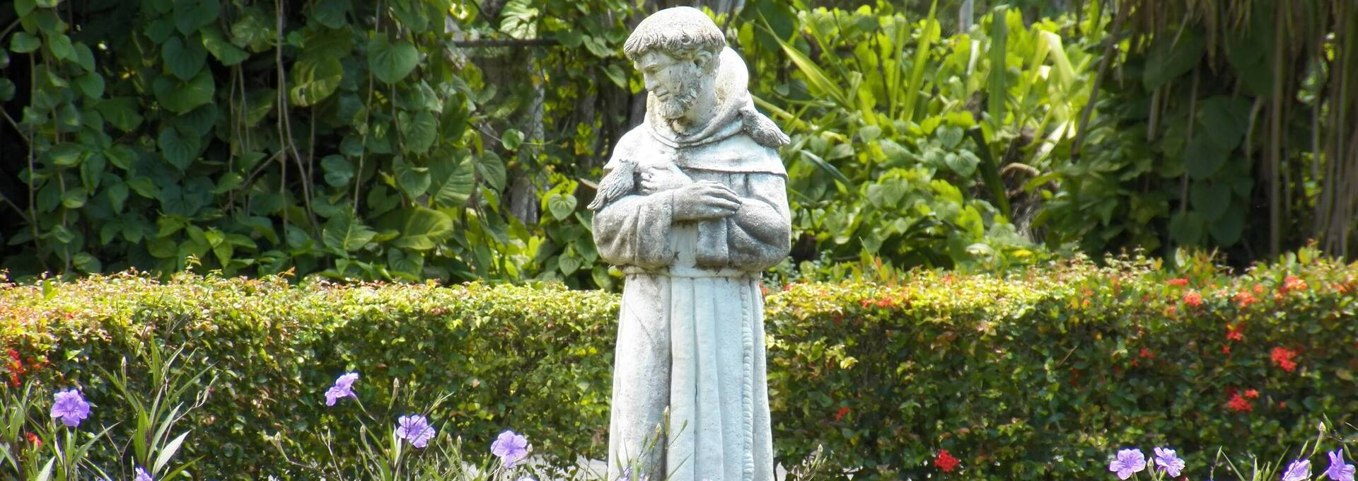 Eine Statue des hl. Franziskus von Assisi inmitten von Blumen und Bäumen