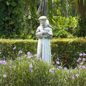 Eine Statue des hl. Franziskus von Assisi inmitten von Blumen und Bäumen