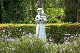 Eine Statue des hl. Franziskus von Assisi inmitten von Blumen und Bäumen